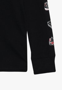 Schwarzes Langarmshirt mit glatter Oberfläche und aufgedruckten Sneakersgrafiken in Weiß und Rot entlang des Ärmels. Einfaches Rundhalsdesign.