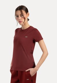 T-shirt a maniche corte color bordeaux realizzato in morbido cotone, con scollatura rotonda e una piccola toppa con logo sul petto.