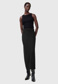 Zwarte mouwloze top gecombineerd met een lange zwarte gebreide rok. De outfit heeft een getailleerd ontwerp en wordt aangevuld met zwarte spitse hoge hakken.