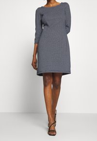 Marinblå klänning med trekvartsärmar, figursydd bodice och utsvängd nederdel. Har ett strukturerat mönster och en bred rund halsringning.