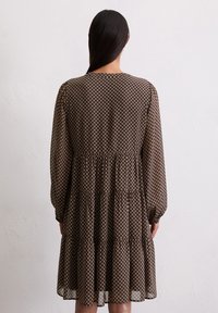 Robe marron à motif, avec des manches longues, une jupe à volants et un décolleté rond. Fabriquée en tissu léger et transparent avec une texture subtile.
