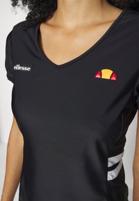 Svart atletisk skjorta med V-hals, prydd med en vit "ellesse"-logotyp och en färgad logopatch i röd, gul och svart på bröstet.