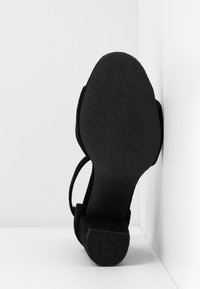 Chaussure à talons hauts en daim noir avec une semelle texturée, dotée d'un talon bloc, d'un bout ouvert et d'un design de fine sangle de cheville.