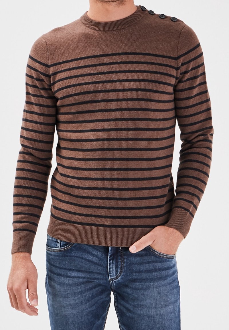 Brauner Strickpullover mit horizontalen schwarzen Streifen, Rundhalsausschnitt und Knopfakzenten an der Schulter, kombiniert mit blauen Jeans.