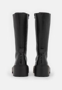 Black leather knee-high boots with a chunky sole, featuring zipper details and embossed branding on the back. Smooth texture and sleek design.