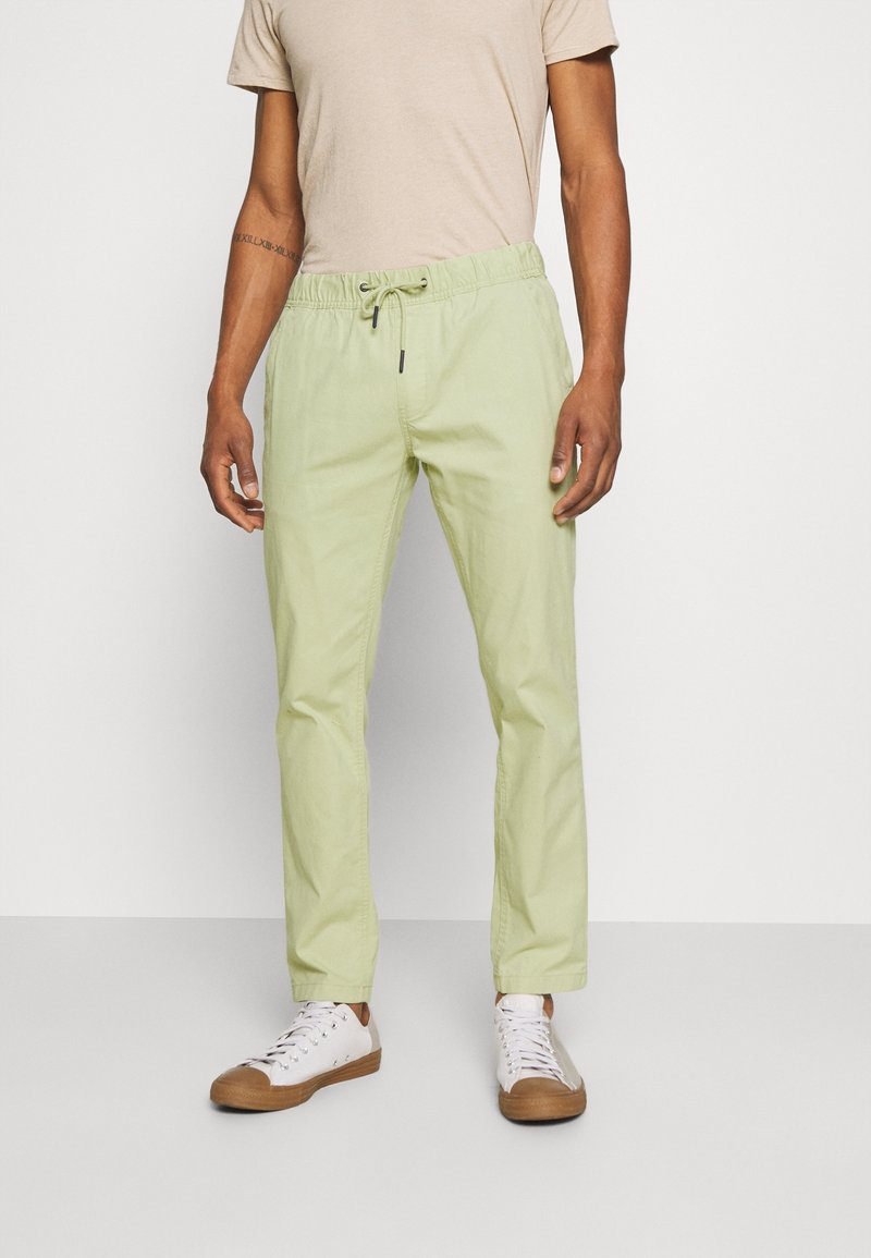 Light green, lightweight pants with an elastic waistband and drawstring, featuring a relaxed fit. Paired with white sneakers and a beige shirt.