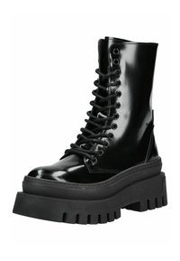 Botas de combate de charol negro con cordones, con una suela de goma negra gruesa, que cuentan con puntera redonda y ojetes metálicos para los cordones.
