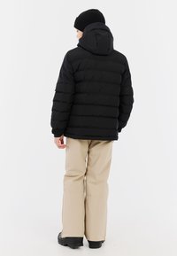 Schwarze Pufferjacke mit horizontalen Steppnähten, verstellbarer Kapuze und elastischen Bündchen, kombiniert mit beigen Hosen und schwarzen Stiefeln. Schlichtes Design, keine Muster.