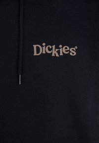 Black hoodie made of soft fabric, featuring a large "Dickies" logo in beige on the chest, with a drawstring and silver aglet.