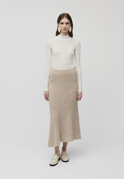 Bluză lungă cu mâneci, cu dungi cremoase, combinată cu o fustă bej, pufoasă, de lungime medie și loafers de culoare deschisă. Design minimalist și texturi moi.