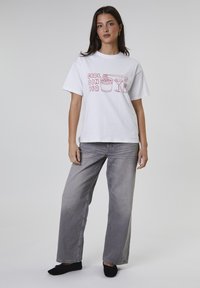 Witte katoenen t-shirt met een grafische print met de tekst "GIRL DINNER" en illustraties van eten en een drankje. Gekleed met lichtgrijze wijde jeans.