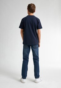 Marineblauw T-shirt met korte mouwen, gemaakt van katoen, gecombineerd met blauwe denim jeans. De jeans hebben een traditioneel zakontwerp en worden gedragen met witte sneakers.