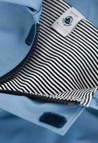 Lichtblauwe waterdichte stof met een zwart-witte gestreepte voering. Voorzien van een ritssluiting en een klittenbandtab voor sluiting. Etiket aanwezig aan de binnenkant.