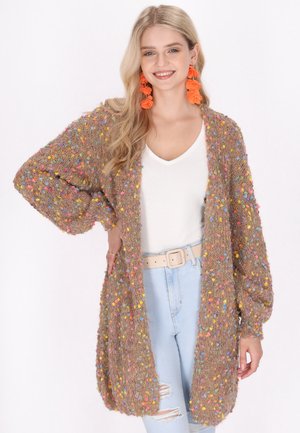 Brown, fuzzy cardigan featuring colorful, bobble-like accents throughout. Loose, oversized fit with wide sleeves. Paired with a white top and light jeans.