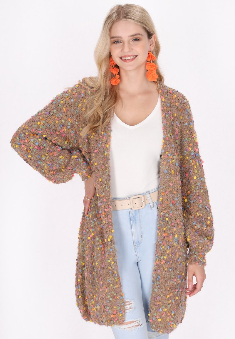Brun, lurvig cardigan med färgglada, bollar-liknande detaljer genom hela plagget. Löst, oversized passform med vida ärmar. Matchas med en vit topp och ljusa jeans.