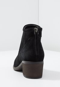 Mustat mokkanahkaiset nilkkasukat, joissa on pyöreä varvas, teksturoitu päällinen, korko ja takana vetoketj yksityiskohta. Hiukan kohotettu puukorko.