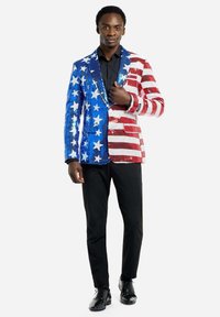 Paillettenblazer met rode en witte strepen aan de ene kant en blauw met witte sterren aan de andere kant; gecombineerd met zwarte broeken en schoenen.