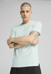 Mjint zeleno kratkolinijsko športno majico z teksturirano površino, ki ima okroglo ovratnico in razdeljen rob, v kombinaciji s temnimi kratkimi hlačami.