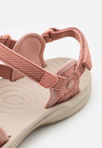 Rosa sandaler med texturerade remmar, justerbara spännen och en formad ljusbeige fotbädd med vågiga mönster för bra grepp.
