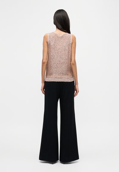 Πλεκτό αμάνικο τοπ σε ανοιχτό ροζ με υφή μοτίβου, συνδυασμένο με φαρδιά μαύρη παντελόνα, με εφαρμογή κομμένη και λείο ύφασμα.