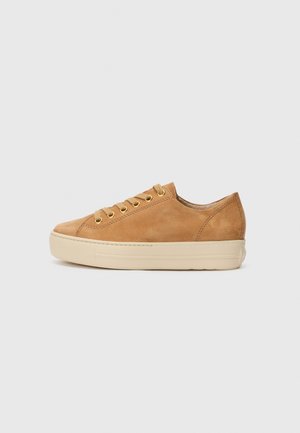 Zapatilla baja de ante color camel con suela de goma beige y cordones a juego sobre un fondo liso de color gris claro.