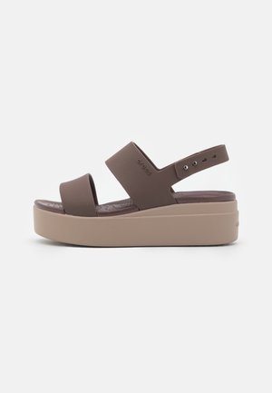 Braune Plateausandalen mit zwei breiten Riemen und einem verstellbaren Fersenriemen. Gepolstertes Fußbett und eine beige Gummisohle.