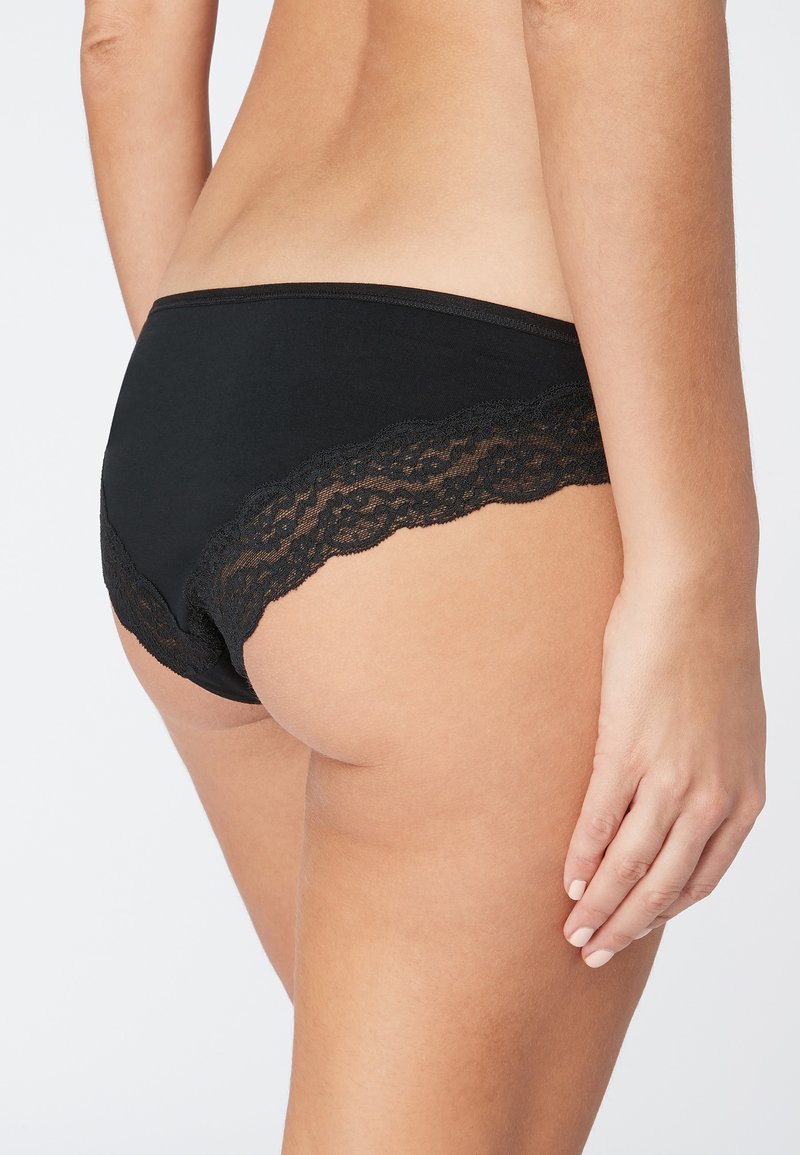 Culottes noires avec dentelle, finition lisse, présentant des bords festonnés et un tissu doux. La vue latérale souligne le design élégant.