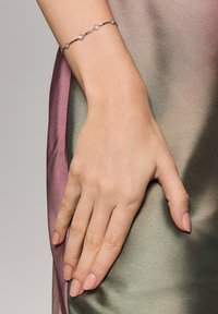 Srebrna bransoletka z pięcioma kwiatowymi akcentami, gładki design, noszona na dłoni na tle gradientu zielonego i fioletowego satynu.