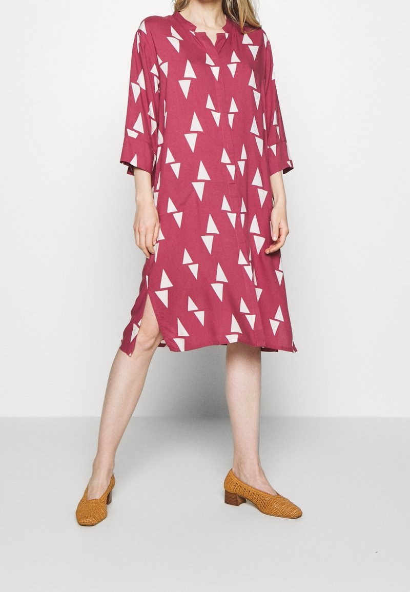 Bordeaux klänning med vita triangulära mönster, knappfront, utan krage, trekvartslånga ärmar, sidoklyvningar, kombinerad med vävda senapsgula klackar.