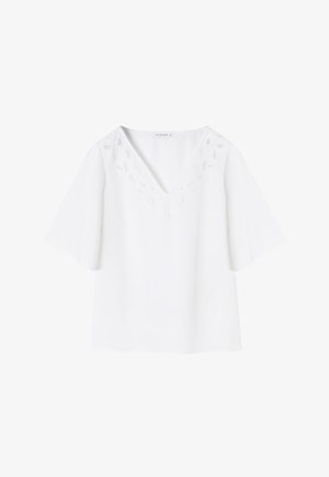 Valge pluus, millel on V-kujuline kaelus, lühikesed eesriide varrukad ja keeruline tikand kaeluse ümber. Sile tekstuur.