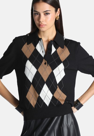 Femme portant un pull noir à manches courtes avec un motif losange marron, blanc et noir, une jupe en cuir noire, des boucles d'oreilles dorées et des bracelets noirs.