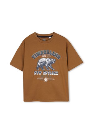T-shirt Timberland marron avec un motif ours bleu et blanc et le texte Timberland, New England, NH U.S.A et unlimited adventure.