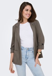 Blazer rayé gris avec manches retroussées, associé à un t-shirt blanc et un jean bleu clair. Comprend un détail avec un seul bouton et des poches avant.