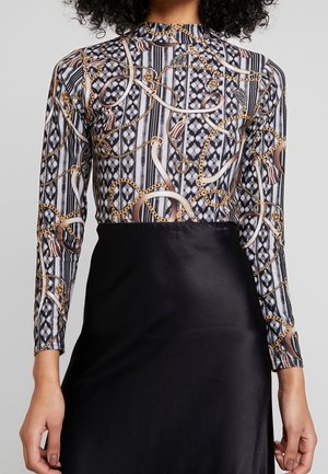 Maglietta a maniche lunghe con un design a strisce bianco e nero decorato con catene, accentuata da un tessuto nero solido nella parte inferiore.