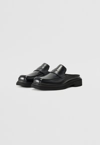 Zapatillas de cuero negro tipo mule con punta redonda, acabado liso, suela de plataforma baja y detalle de tira minimalista en la parte superior.