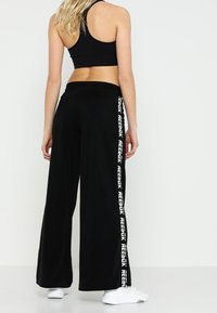 Pantalones de pierna ancha negros hechos de un material suave, con una marca blanca a lo largo del costado. La cinturilla es elástica para mayor comodidad.