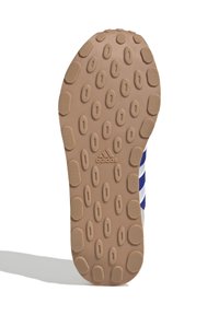 Brązowa gumowa podeszwa z heksagonalnymi i owalnymi wzorami, z logo Adidas. Projekt zawiera niebieskie i białe paski po bokach.