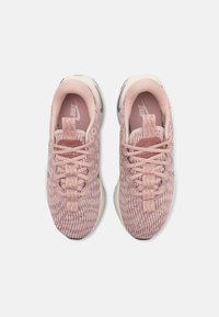 Nike idrettssko i lys rosa med en teksturert overdel i stoff, strikkedesign, flate lisser og en myk hvit mellom såle.