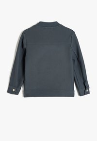 Mörkgrå ribbad jacka med långa ärmar, knäppta manschetter och ett kragfritt design. Texturerad tyg med ett horisontellt randmönster.