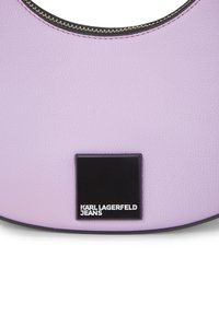 Bag em imitação de pele lavanda com um design circular, apresentando um patch de logotipo retangular preto. Detalhe com zíper ao longo da borda superior.