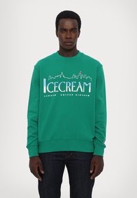 Grøn sweatshirt med rund hals, prydet med "ICECREAM" tekst og skyline grafik i blå og hvid, samt "London United Kingdom" trykt nedenfor.