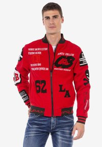 Rote Bomberjacke mit verschiedenen schwarzen und weißen Texten und Grafiken. Sie verfügt über einen vorderen Reißverschluss und gestreifte Bündchen und Saum.