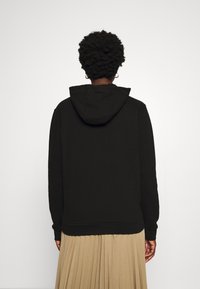 Černá mikina s kapucí a volným střihem, texturovaná látka a žebrované manžety, v kombinaci s plisovanou béžovou sukní.