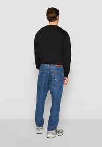 Sort sweatshirt, blå denim jeans med baglommer og grå sneakers, set fra bagfra. Glat stof og løs pasform.