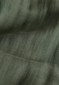 Prim-plan al unui material verde închis texturat, cu un model subtil în zigzag diagonal și cute moi vizibile.