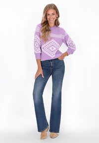 Lila trui met witte geometrische patronen, gecombineerd met blauwe flare jeans en beige laarzen, wat zorgt voor een casual outfit.