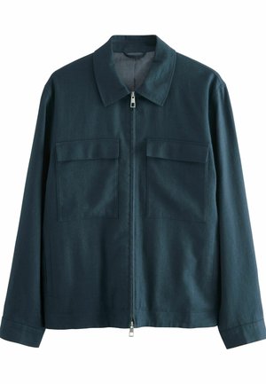 Giacca a zip di color teal scuro realizzata in un tessuto texturizzato. Presenta un colletto a punta e due tasche sul petto con pattina. Maniche lunghe con polsini a bottone.
