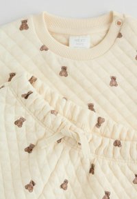 Quiltede cremede baby pyjamas med små brune teddy-bjørn prints, med en ribbet krave og en elastisk talje med snoretræk.