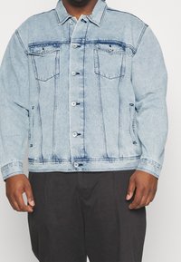 Vaaleansininen denim-takki, jossa on nappisuljenta, kaksi rintataskua ja sivutaskut. Sisältää haalistuneita alueita ja kontrastiväriset ompeleet.