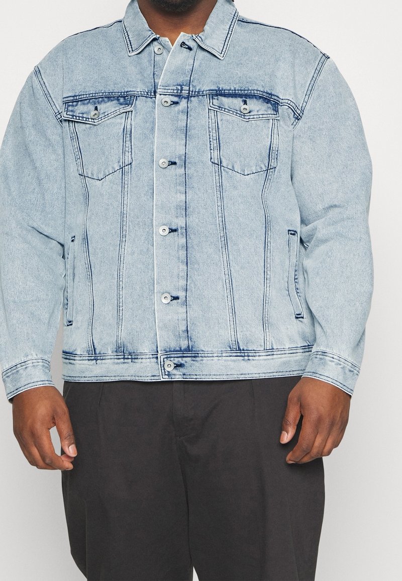 Vaaleansininen denim-takki, jossa on nappisuljenta, kaksi rintataskua ja sivutaskut. Sisältää haalistuneita alueita ja kontrastiväriset ompeleet.